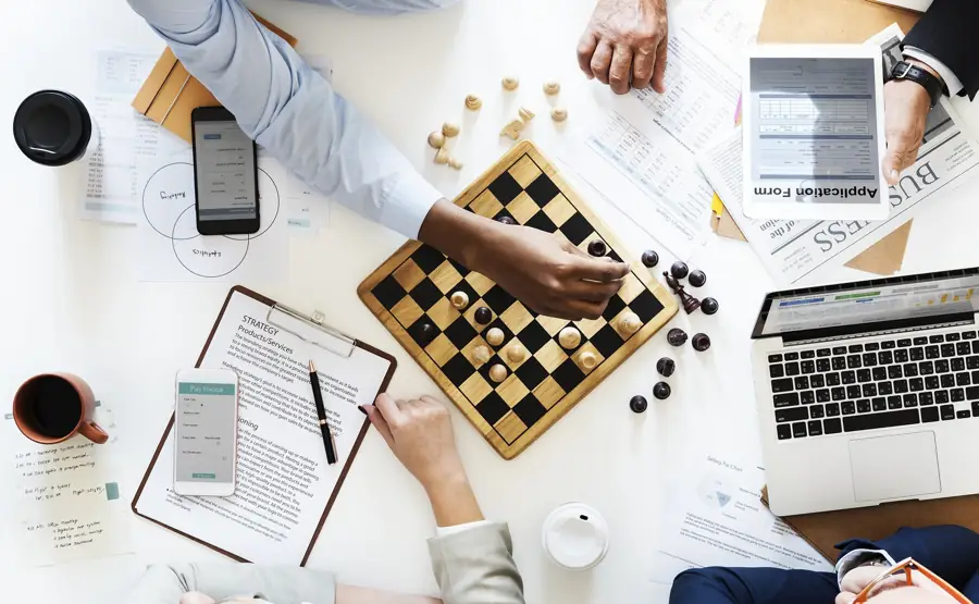 Desk from above with a chess board, financial documents and a laptop