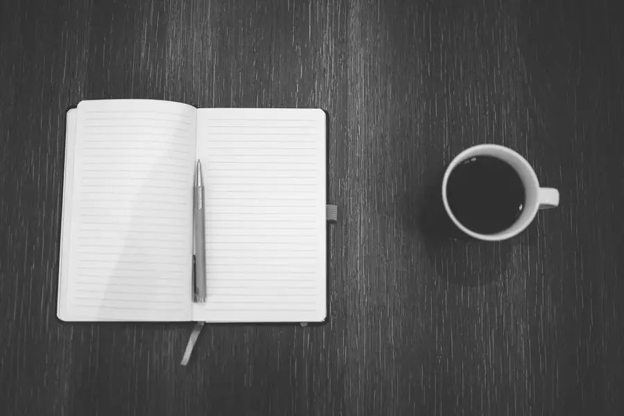 Open notebook and pen beside a cup of coffee on a dark desk