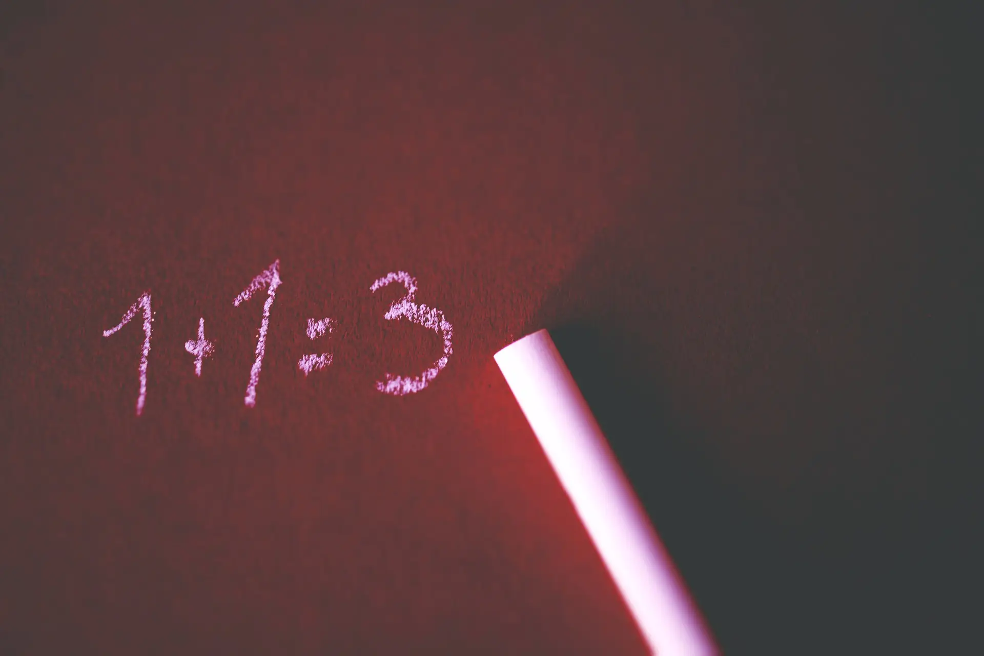 One plus one equals three written in chalk on a blackboard