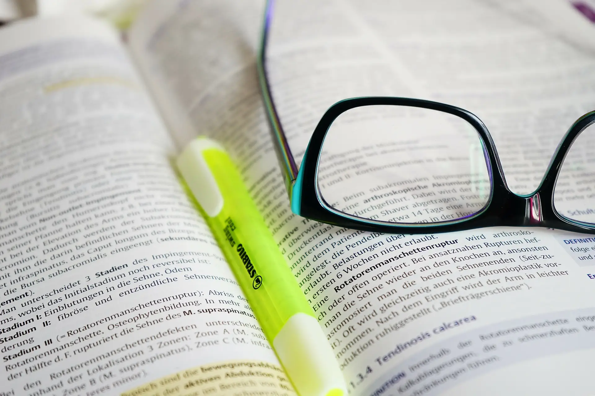 Reading glasses and a highlighter resting on an open book